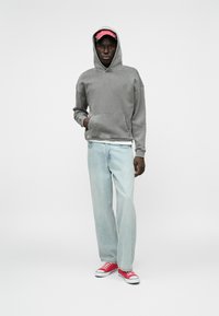 Γκρι φούτερ με μπροστινή τσέπη, ανοιχτό μπλε τζιν ίσιου κοψίματος και κόκκινα αθλητικά παπούτσια. Το φούτερ έχει κορδόνι και καγκουρό τσέπη.