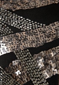 Tissu en maille noire orné de sequins géométriques métalliques et de perles argentées et bronzes, disposés en motifs tourbillonnants créant des couches texturées.