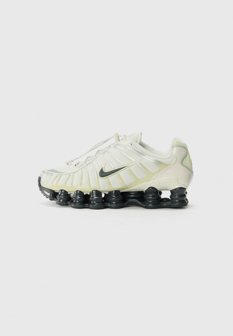 Baltie un gai zaļie Nike apavi ar strukturētu virsmu, redzamām šņorēm un melnu segmentētu zoli, ar atstarojošiem akcentiem.