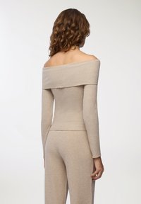 Beżowy, prążkowany top bez ramiączek z długimi rękawami i dopasowanym krojem. Miękki materiał o delikatnym blasku, w połączeniu z pasującymi spodniami.