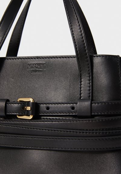 Sac à main en cuir noir au design structuré. Présente des détails en métal doré, un logo en relief et une texture lisse. Deux poignées avec des détails de couture.