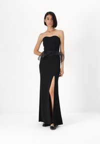 Vestido preto sem alças com forma ajustada, fenda lateral e um detalhe na cintura em tule preto. Textura suave com um design elegante e minimalista.