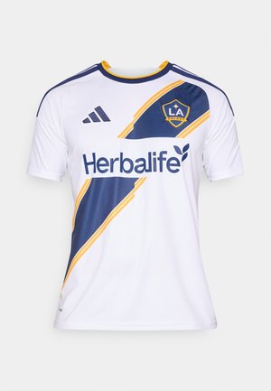 Λευκή ποδοσφαιρική φανέλα με μπλε και κίτρινα διαγώνια στοιχεία, με το λογότυπο "Herbalife" και το έμβλημα της "LA Galaxy". Κατασκευασμένη από αναπνεύσιμο ύφασμα.