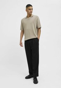 Beige polo shirt met korte mouwen en een zachte textuur, gecombineerd met loose-fit zwarte broek. Zwarte schoenen maken de outfit compleet.
