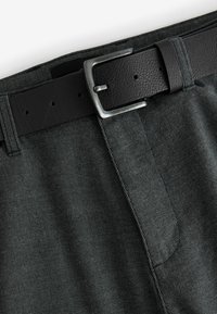 Pantalons légers gris à carreaux avec une ceinture en cuir noir, dotée d'une boucle rectangulaire en argent et de détails de couture visibles.