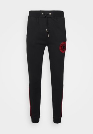 Schwarze Slim-Fit-Jogginghose mit elastischem Bund, Kordelzug, roten Seitenstreifen und einem runden roten Emblem am rechten Oberschenkel.