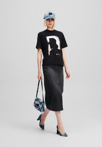 Melna t-krekls ar metālisku siluetu grafiku, saskaņots ar tumšu džinsu svārku. Aksesuāri ietver zilu džinsa cepuri un atbilstošu somu.