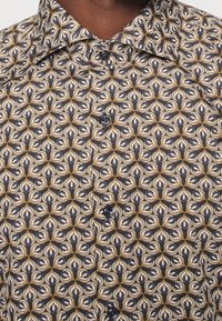 Overhemd met patroonknoopsluiting en een geometrisch ontwerp in marineblauw, beige en goudtinten. Gemaakt van gladde stof, met twee zichtbare knopen.