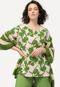 Top verde con motivo floreale e scollatura a V, abbinato a un cardigan a strisce verde e crema, indossato sopra pantaloni verdi a trama.