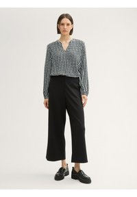 Blusa blanca y negra con estampado y escote en V, combinada con pantalones de pierna ancha negros de cintura alta y zapatos negros gruesos. Texturas suaves.