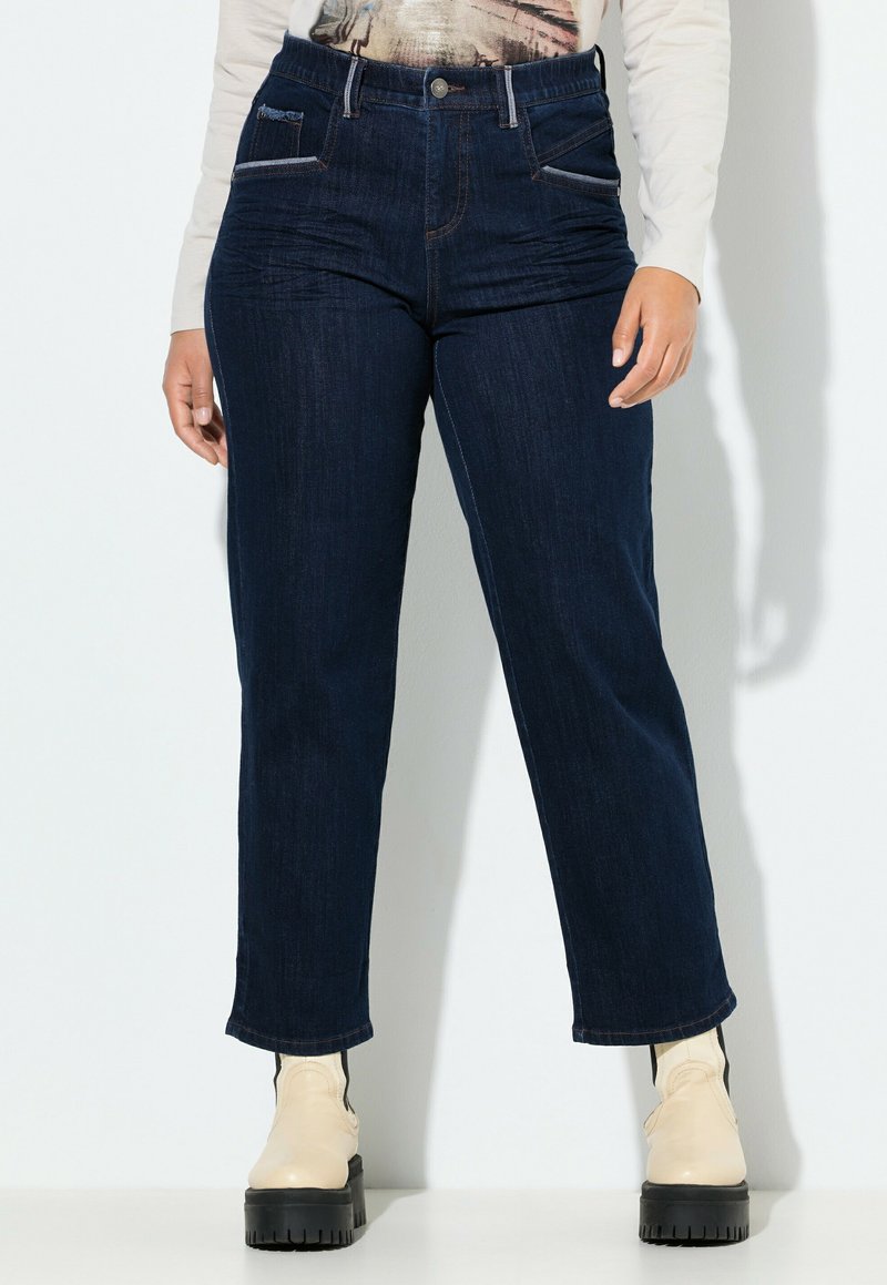 Jeans de mezclilla oscuros con una cintura alta, diseño de pierna recta, costuras en contraste y bolsillos delanteros. Combinados con botas hasta el tobillo.