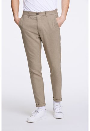 Beige patterned trousers with a tailored fit, featuring a button closure and side pockets, paired with white sneakers.