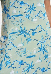 Tessuto verde chiaro con motivo tropicale blu, che presenta palme, nuvole, barche e il testo "Just Rhyse" in diverse dimensioni.