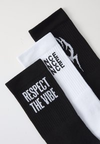 Three pairs of socks: one black with "RESPECT THE VIBE" in white, one white with black accents, and one solid black. Ribbed texture throughout.