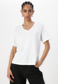 Hvid bomulds T-shirt med v-hals, korte ærmer og løs pasform. Har diskret logo broderi på venstre bryst.