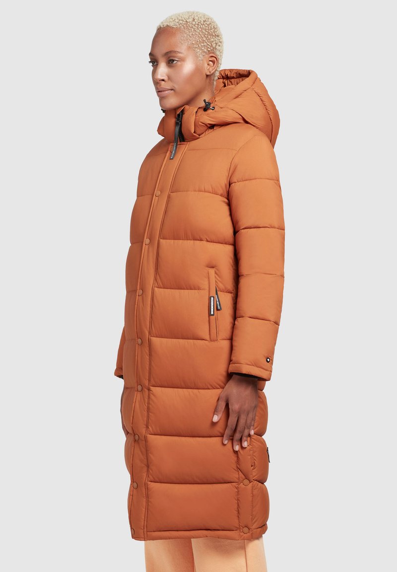 Langer, puffer Mantel in verbranntem Orange mit Kapuze. Verfügt über ein kastiges, gestepptes Design, seitliche Taschen und Druckknopfverschlüsse. Strukturierter Stoff.