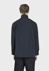 Tmavě námořnická bunda s stojáčkovým límcem, dlouhými rukávy a manžetami na knoflíky. Má jednoduchý design bez vzorů nebo viditelného kovového hardware.