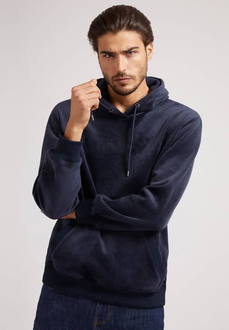 Sudadera con capucha de felpa azul marino con cordón y logo bordado en el pecho. Puños y cintura acanalados con una textura suave.