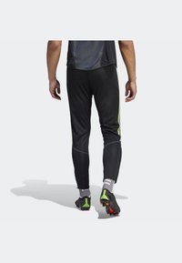 Černé sportovní kalhoty s přiléhavým střihem, neonově zelené boční pruhy, elastický pas a zúžené nohavice. Nosit se fotbalovými kopačkami.