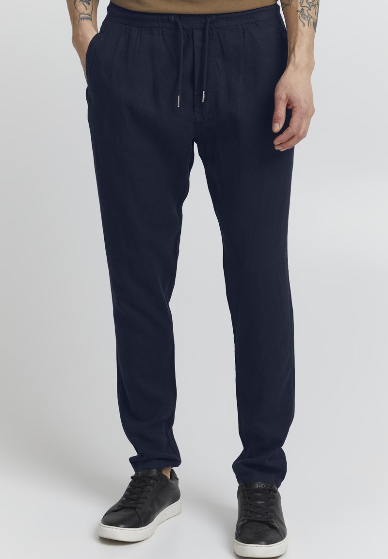 Mörkblå linbyxor med elastisk midja och dragsko, med sidofickor och smal passform, tillsammans med svarta sneakers.