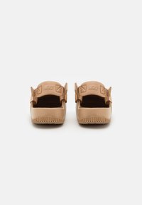 Las sandalias Nike de deslizamiento en color beige presentan un diseño moldeado con parte trasera abierta, suelas texturizadas y correas ajustables con detalles de logotipo.