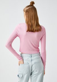 Różowa, prążkowana bluzka z długim rękawem o kroju cropped, zestawiona z jasnoniebieskimi jeansami z wysokim stanem i tylnymi kieszeniami. Gładka faktura.