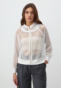 Giacca bianca in rete con zip, colletto scallopato, polsini a coste e un orlo aderente; presenta una zip dorata e una texture leggera.