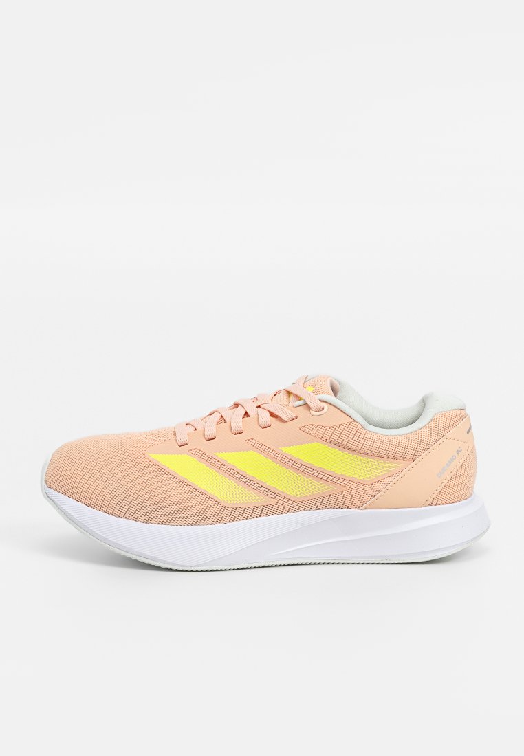 Zapatilla deportiva de color rosa claro con parte superior de malla, acentos amarillos y suela de goma blanca. Presenta un diseño aerodinámico y cierre con cordones.