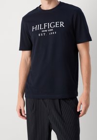 Navy blue cotton T-shirt featuring a white printed logo "HILFIGER NEW YORK EST. 1985" across the chest. Short sleeves and crew neckline.