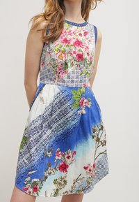 Kukkakuvioinen lyhyt mekko sinivalkoisissa sävyissä, jossa on istuva yläosa ja levenevä helma, pyöreä pääntie ja kontrastisauma.