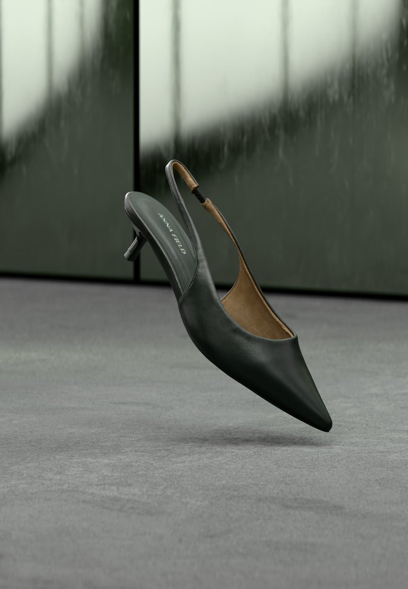 Μαύρο γυναικείο παπούτσι με ακρυβολέκτη μύτη και λεπτό λουράκι τύπου slingback, με τακούνι kitten και ετικέτα "ANNA FIELD" στην εσωτερική σόλα, σε θολό γκρι φόντο.
