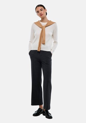 Pull en tricot crème clair, écharpe camel nouée au cou, associé à un pantalon large gris foncé et des chaussures noires à lacets. Design simple et cohérent.
