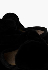Zapatillas negras hechas de material de felpa, con bordes redondeados y suaves detalles de pompón, y un forro interior texturizado.