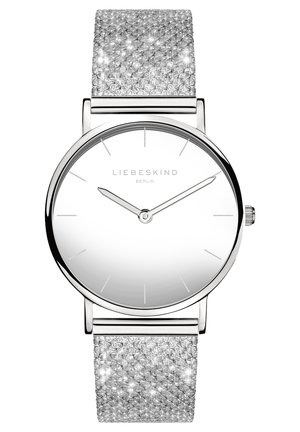 Montre argentée avec un cadran rond et un bracelet en maille scintillante. Le cadran est blanc avec des marqueurs d'heure minimalistes et deux fines aiguilles argentées.