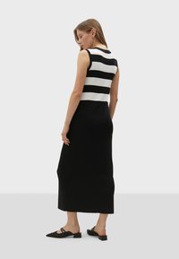 Czarnobiała, paskowana, bezrękawnikowa sukienka dzianinowa, z dopasowanym topem i zwiewnym dołem. Materiał wydaje się gładki o miękkiej teksturze.