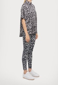 Camicia a maniche corte con stampa leopardata e leggings in bianco e nero, abbinati a sneakers bianche. La parte superiore presenta un colletto.