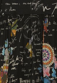 Czarna tkanina z białym, odręcznym tekstem, kolorowymi motylami i koliberkami oraz wielokolorowym mandalą ozdobioną cekinami.