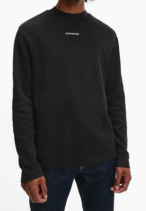 Pull noir avec un col rond, des manches longues et un logo blanc "CALVIN KLEIN JEANS" sur la poitrine. Texture douce et poignets côtelés.