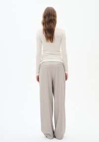 Light beige long-sleeve top and light grey wide-leg trousers. Trousers feature pockets and subtle texture. Model facing away, neutral background.