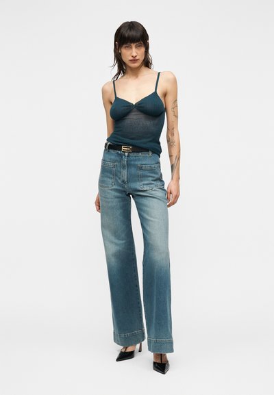 Τιρκουάζ ριμπ τοπ με λεπτές τιράντες, συνδυασμένο με φαρδιά παντελόνια σε ξεθωριασμένο μπλε και μαύρες ψηλοτάκουνες γόβες. Μινιμαλιστικός σχεδιασμός, casual εφαρμογή.