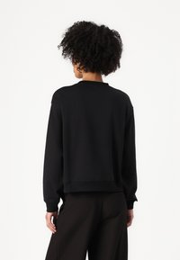 Felpa nera con una vestibilità ampia, polsini e orlo a costine, e scollo rotondo. Tessuto morbido con una texture liscia, design minimalista.