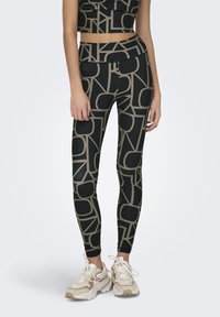 Zwarte leggings met een geometrisch beige patroon, hoog in de taille, gemaakt van rekbaar materiaal, gecombineerd met chunky sneakers in neutrale tinten.
