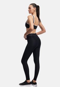 Czarny sportowy stanik i legginsy z wysokim stanem z białymi wykończeniami. Materiał wygląda na elastyczny; legginsy dopasowane do ciała. Model nosi czarne buty do biegania.