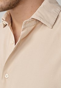Chemise en velours côtelé beige clair avec une texture douce, un devant boutonné et un col replié avec une délicate finition ton sur ton.