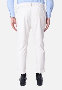 Pantaloni bianchi con vestibilità affusolata, cintura elasticizzata e tasca posteriore singola. I risvolti accentuano il design elegante. Scarpe nere completano il look.