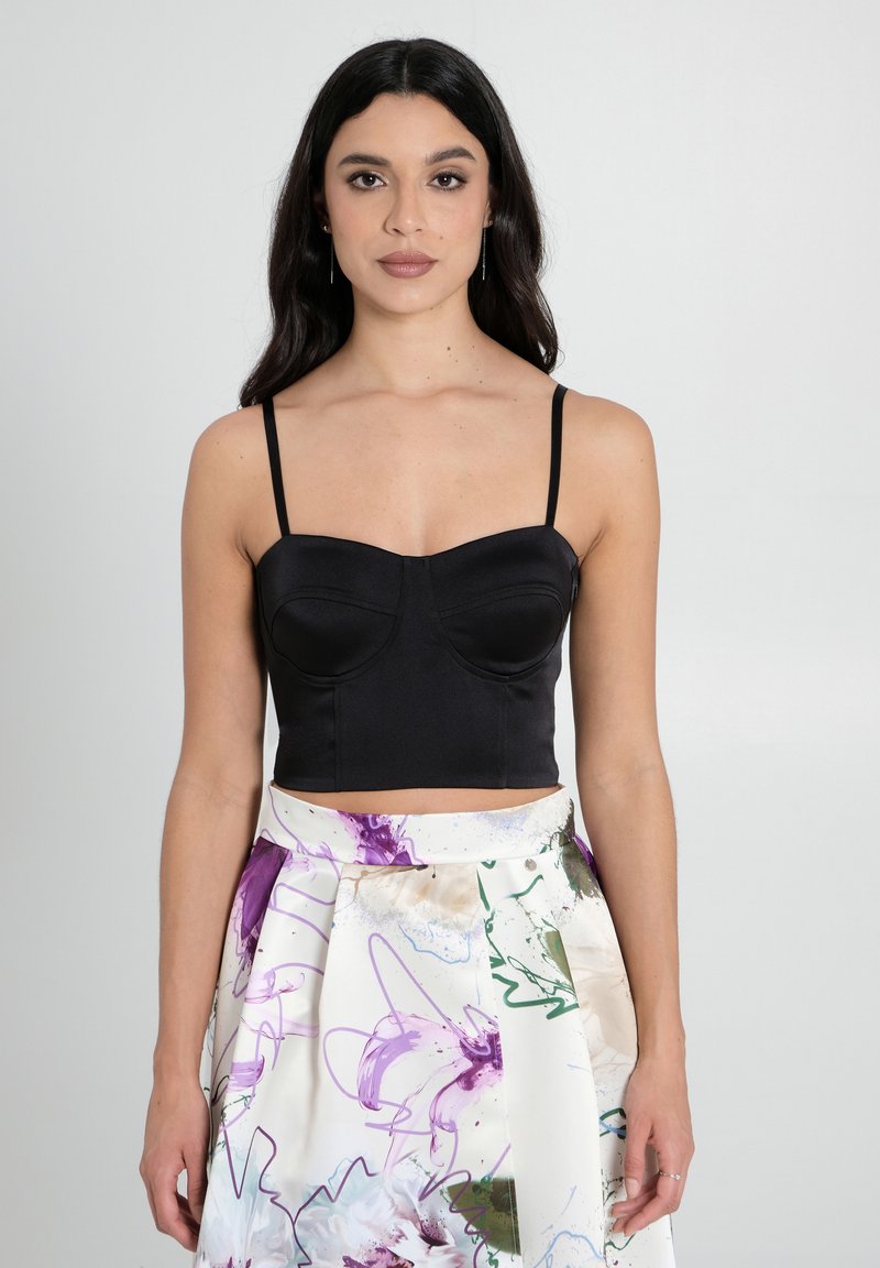 Top cropped di raso nero con coppa strutturata e spalline sottili, abbinato a una gonna con fantasia floreale caratterizzata da accenti viola e verdi.