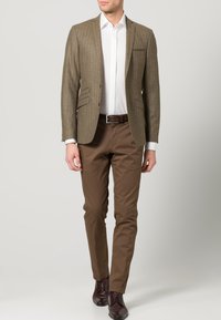 Bruine gestreepte blazer, witte overhemd, bruine chino's en donkerbruine schoenen. Blazer heeft met een notch uitgesneden revers en voorzakken. Schone lijnen en een getailleerde pasvorm.