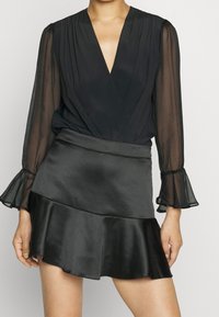 Black sheer long-sleeve blouse with a deep V-neck and pleated details, paired with a black satin flared mini skirt featuring a ruffled hem.
