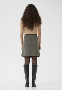 Haut beige à manches courtes, jupe grise en tweed, et bottes noires montantes. La jupe s'évase à l'ourlet avec une texture subtile et une taille haute.