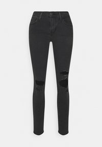 Jeans ajustados negros de mezclilla, con detalles desgastados en las rodillas. Se ven los bolsillos frontales y los lazos para el cinturón. Textura suave.